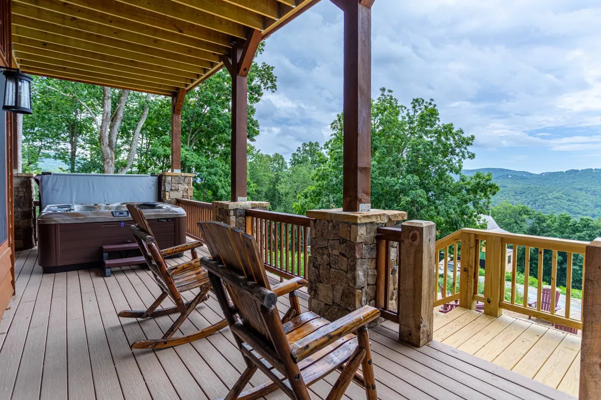 This exterior image features a hot tub and wooden rocking chairs positioned on a deck with a sweeping panoramic view of the surrounding mountains. The scene suggests relaxation, socializing, and an immersive nature experience, perfect for unwinding after a day of activities.