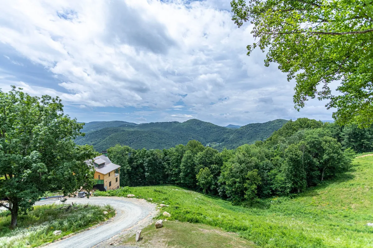 A wide-angle view of the mountain range, with the house nestled among trees and a meandering dirt road. The peaceful landscape hints at the adventure, exploration, and natural beauty surrounding the property.