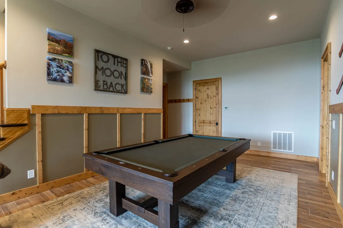 A cozy game room interior where a pool table takes center stage. Warm wooden accents and playful wall art create an inviting space designed for friendly competition and laughter, perfect for evenings spent together after outdoor activities.