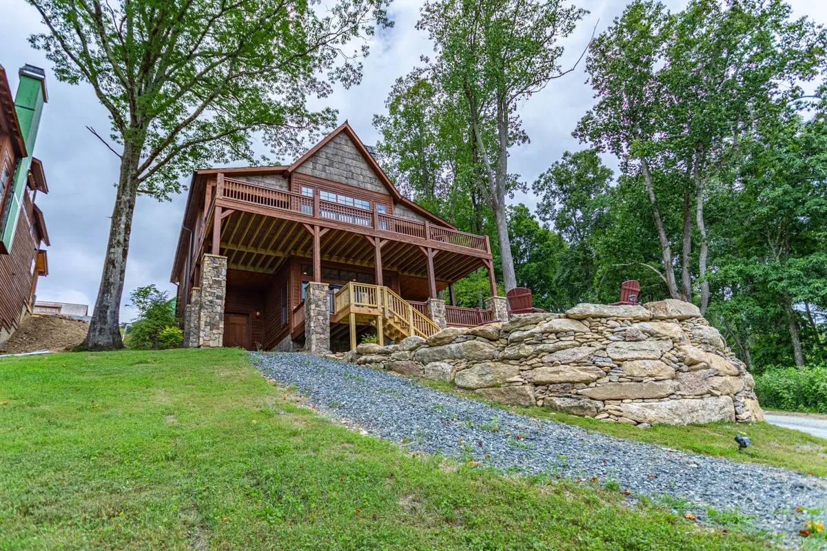A wide view of the home's wooden deck and stone facade, opening onto a landscaped yard ideal for gatherings. The space suggests versatile outdoor use—barbecuing, playing games, or spending time with friends and family—set against a backdrop of natural scenery.