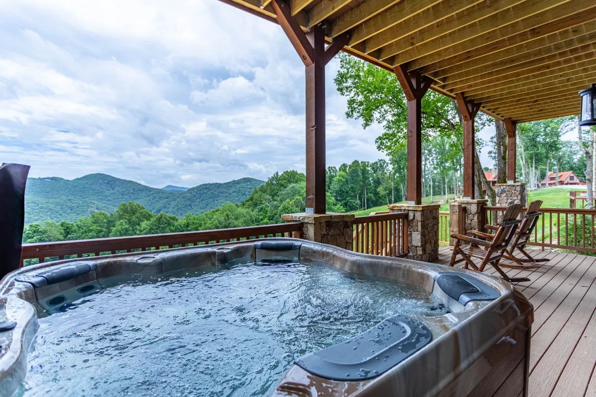 An outdoor deck scene with a sparkling hot tub, wooden rocking chairs, and breathtaking mountain views. The mood is tranquil and inviting, ideal for soaking under the stars or gathering with loved ones after a day of fun.