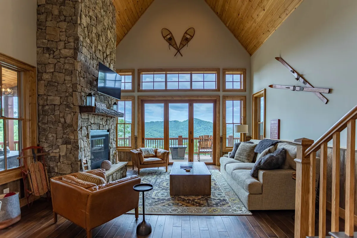 A cozy interior scene showcasing a stone fireplace, rustic furniture, and large windows framing mountain vistas. The space is inviting and serene, ideal for sharing fireside moments or basking in the mountain sunrise.