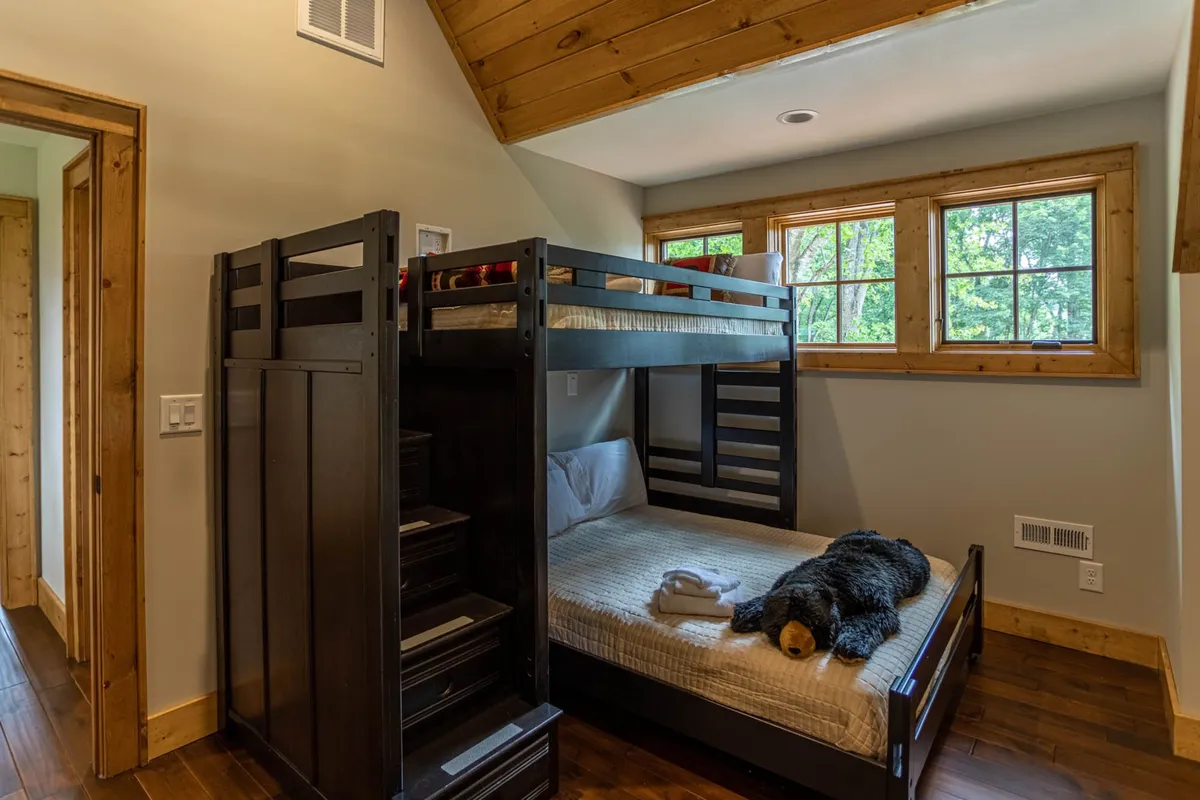 A playful loft area featuring a cozy twin-over-full bunk bed, a teddy bear, and warm wooden accents. The space is inviting, ideal for children or extra guests, and filled with personality.