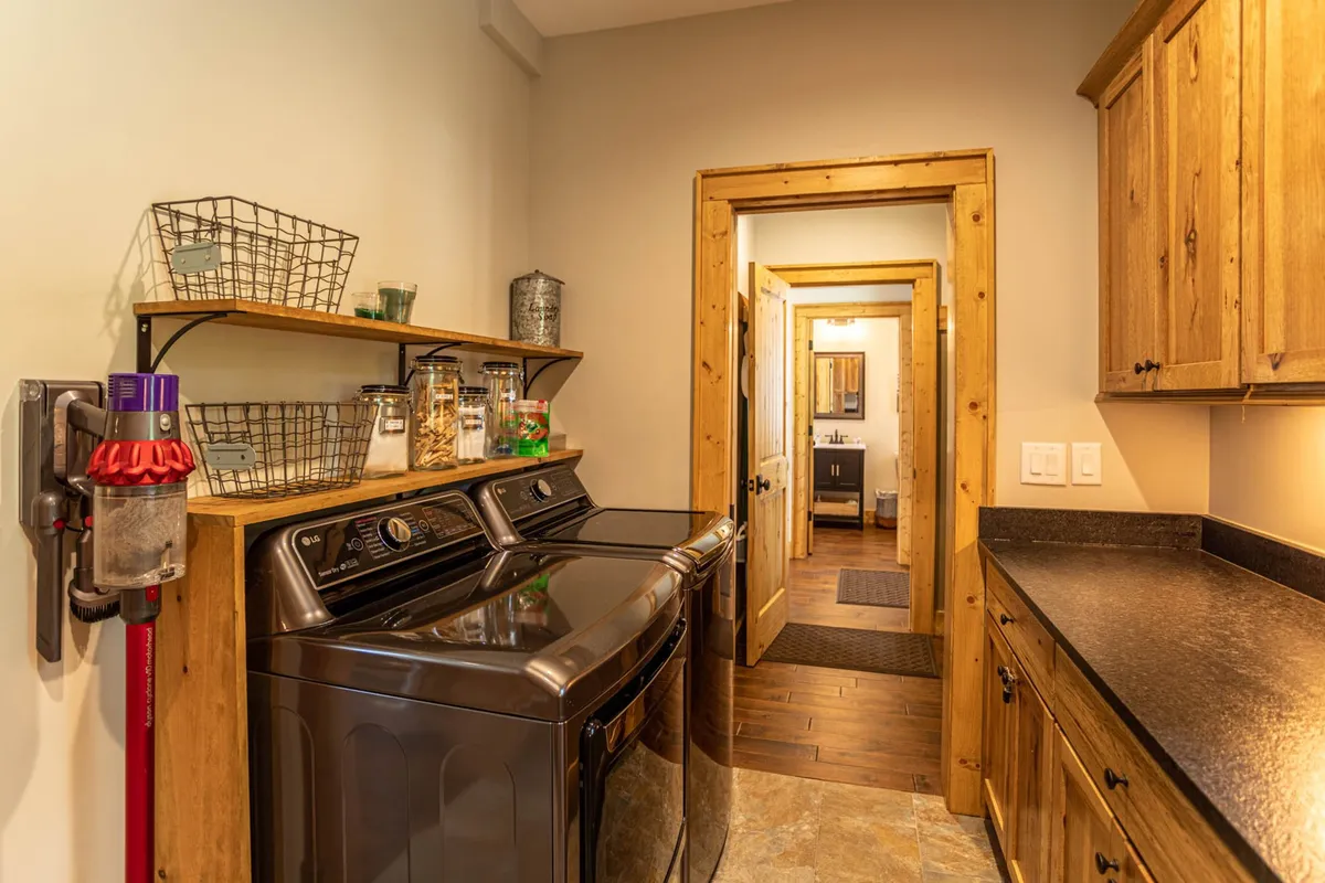 This image highlights the adjacent laundry and workspace, featuring washer and dryer units, wooden shelving, and a welcoming, practical atmosphere. It showcases the convenience and extended-stay readiness of the home.